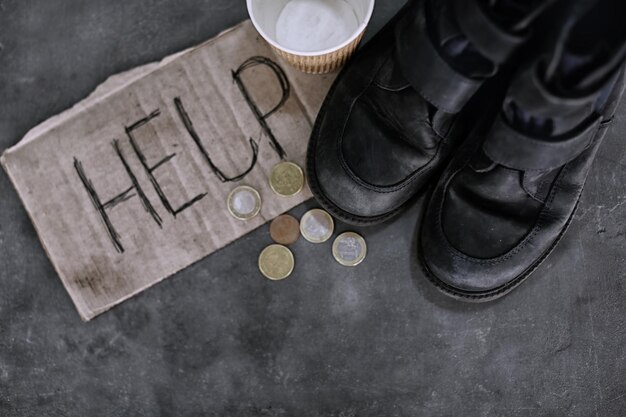 Монеты старой обуви и кусок картона со словом ПОМОЩЬ на сером фоне Концепция бедности