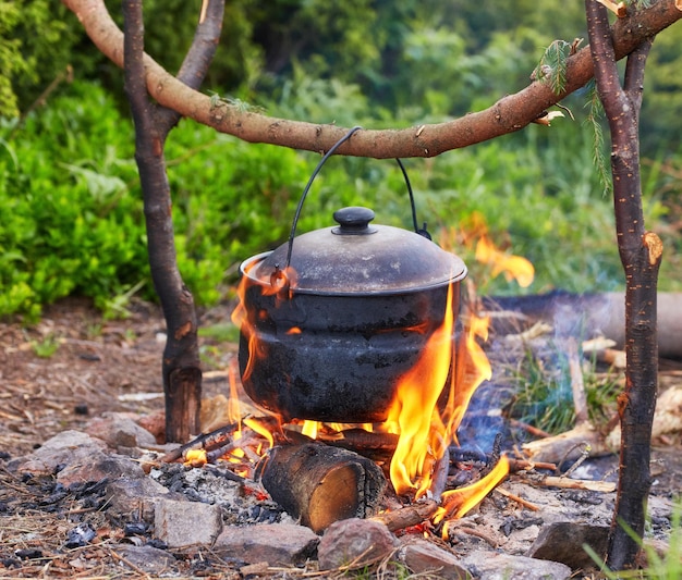 Old small kettle is heated on a bonfire on a green mountain meadow during a bad weather