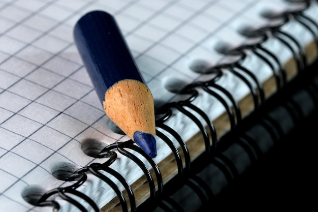 An old small used sharpened blue wooden slate pencil lies on an open checkered notebook, close-up