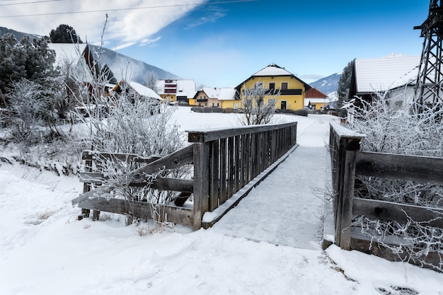 Old small wooden bridge over mountain river in Alps at snowy day