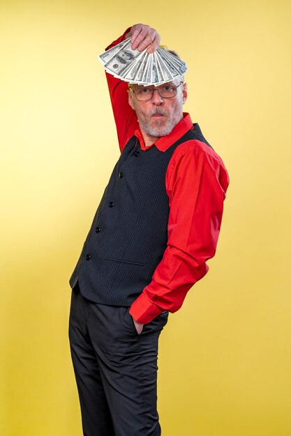 Old smiling grey-haired man in eyeglasses. Holding fan of dollars over head in dancing pose. Human emotions and facial expressions