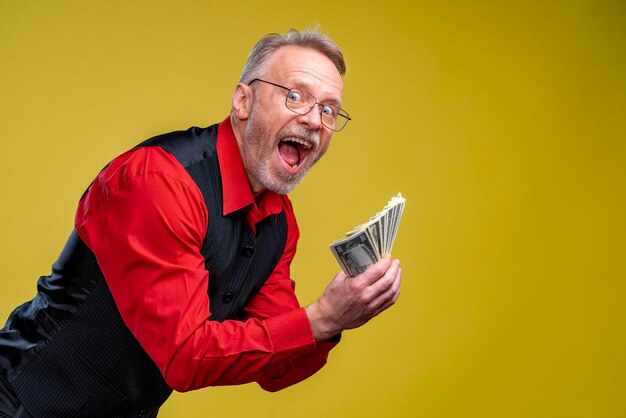 Old smiling greyhaired man in eyeglasses holding fan of dollars in hands Human emotions and facial expressions Half waist portrait