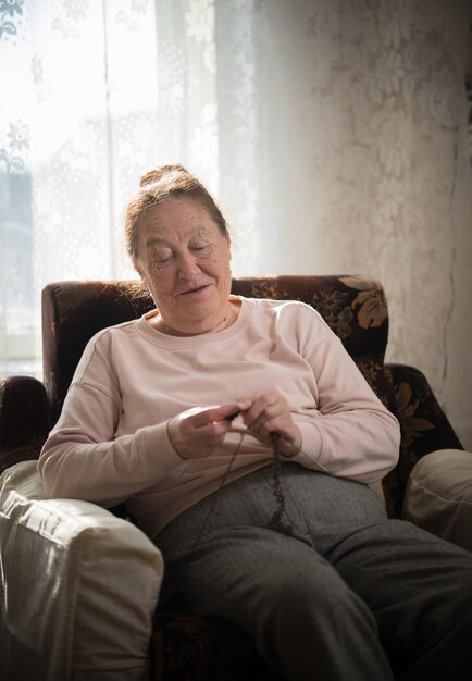 An old smiling woman sitting in the armchair and knitting