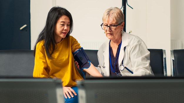 Old specialist using tonometer to measure hypertension on asian\
patient, checking blood and pulse pressure at cardiac test. doctor\
doing cardiology examination at clinic. handheld shot.