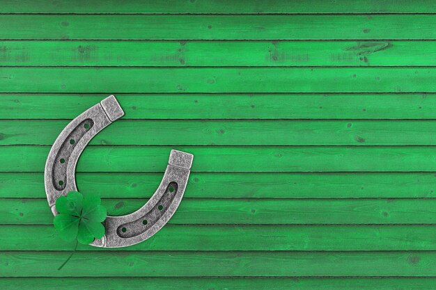 Photo old steel lucky horseshoe with green clover four leaf on a green wooden plank background 3d rendering