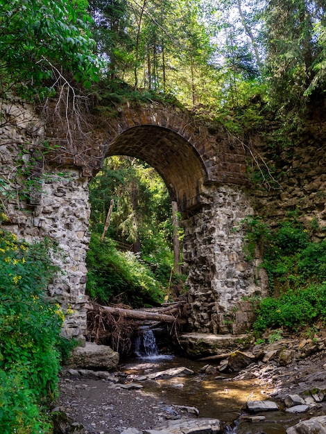 Foto vecchio ponte di pietra ad arco distrutto su un piccolo fiume in una foresta di montagna