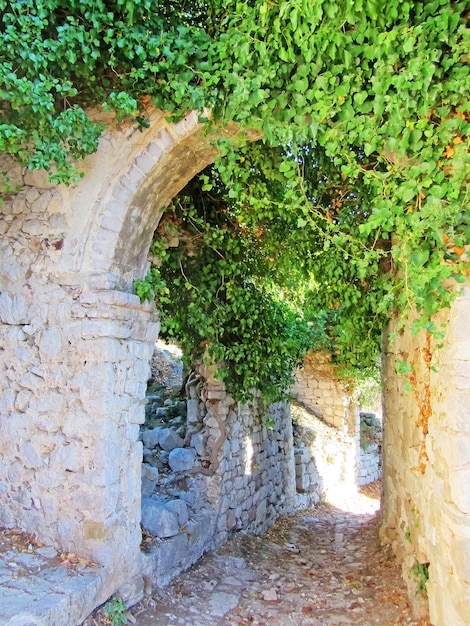 An old stone bridge over a rocky road along which a small stream flows between colorful hills with greenery and flowers