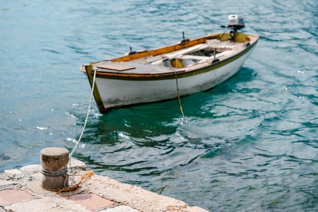 Foto una vecchia bitta di pietra del mare sul molo con una barca da pesca in legno legata