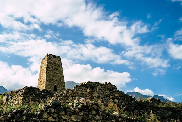 Old stone tower in green mountainous terrain Ancient stone building of old town located on green hill against mountains covered with forest in summer day