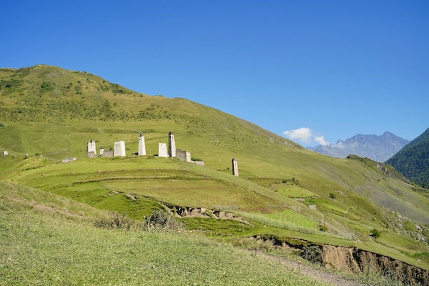 Old stone towers in green mountainous terrain Ancient stone buildings of old town located on green hill against mountains covered with forest and fog in summer day