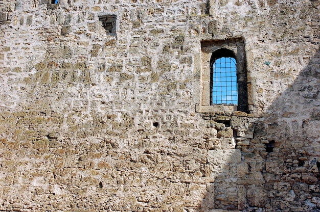 Old stone wall built of limestone bricks with a small window with bars