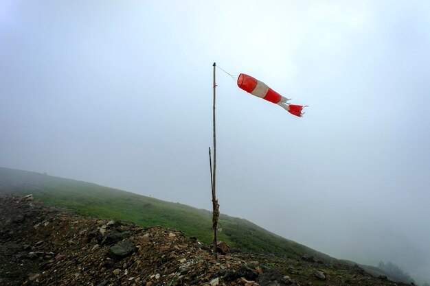 Foto vecchio indice a righe rosso-bianco della forza e della direzione del vento in montagna in nebbia