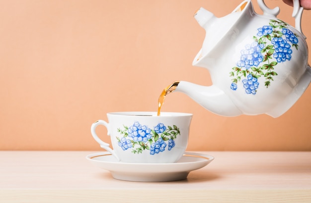 Photo old-style porcelain kettle pouring tea from jug to cup of tea