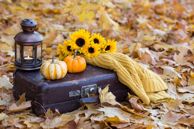  old suitcase, on it two pumpkins, an old lantern with a candle, a bouquet of sunflowers and a knitted yellow sweater 