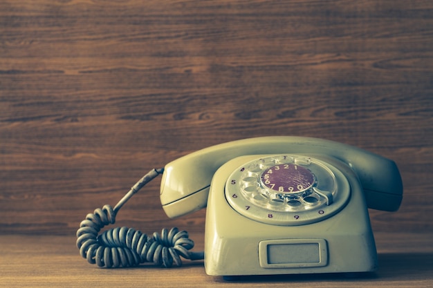 Old telephone on wooden table background. Vintage tone