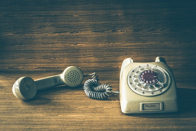 Old telephone on wooden table background. Vintage tone