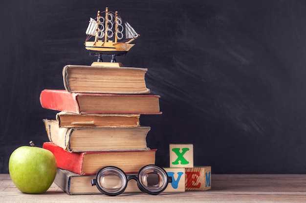 Old textbooks are on the rustic wooden table on a background of black chalk board.