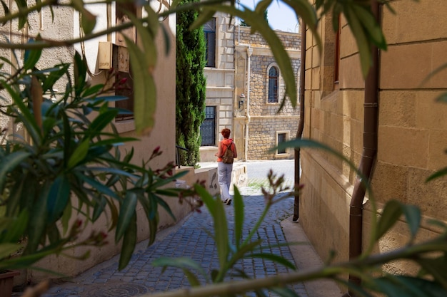 Old town narrow street between carved stone buildings with walking female tourist Baku Azerbaijan