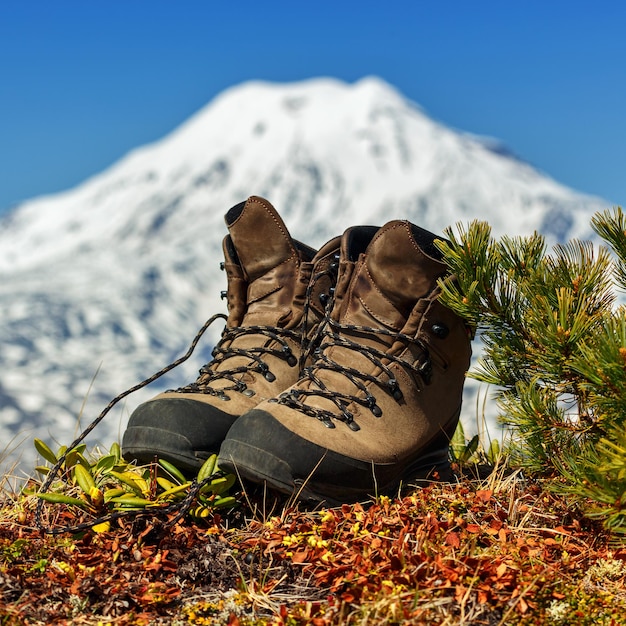 Old trekking boots stand in tundra against background of cone of volcano