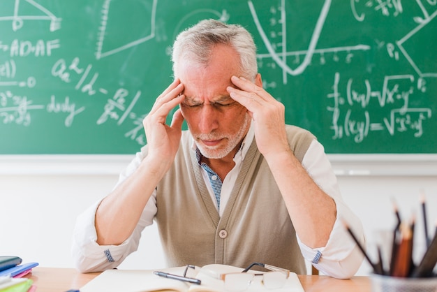 Old tutor with headache in lecture room