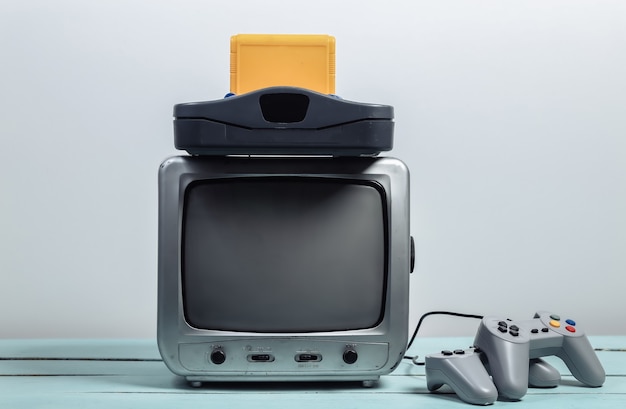 Old tv receiver with retro game console, joysticks on a white wall. Retro gaming