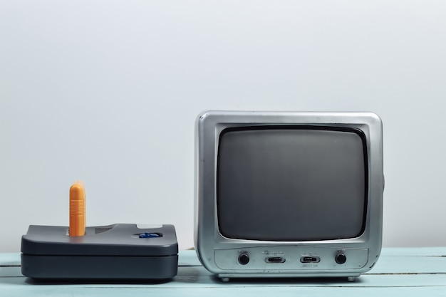 Old tv receiver with retro game console on white wall. Retro gaming