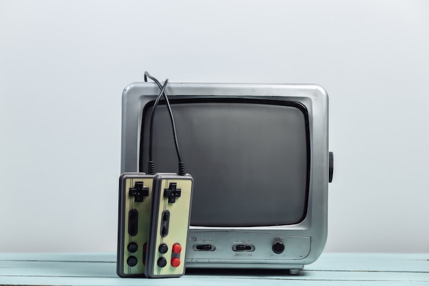 Old tv receiver with retro joysticks on a white wall. Retro gaming.