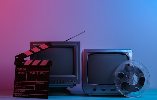 Фото Старые телевизионные приемники с хлопушкой для фильмов, катушка с пленкой в красно-синем неоновом свете. развлекательная индустрия