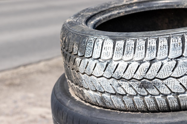 Old used car tires in white paint stacked on top of each other near the tire shop against a blurred ...