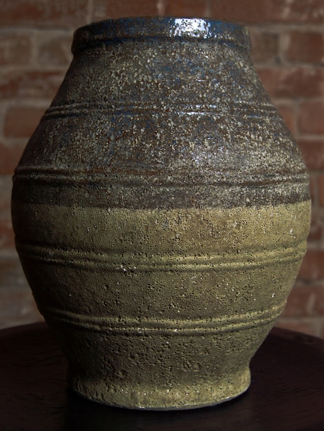 An old vase on a black round table on a brick wall background