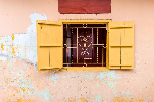 Old vintage yellow beige small window with heart shaped window grill and fall off concrete wall