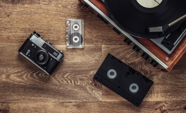 床にある古いビニールレコードプレーヤー、ビデオカセット、オーディオカセット、昔ながらのフィルムカメラ。レトロメディア80年代。上面図