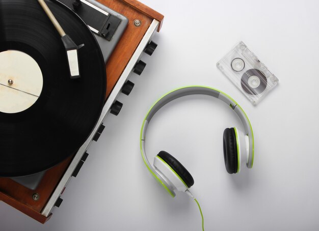 Old vinyl record player with stereo headphones and audio cassette on white surface