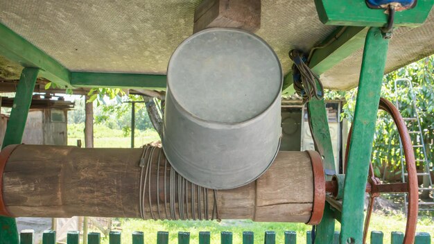 An old water well with a bucket in the garden, a metal handle for lifting water from the ground. Village well under the roof with a rope. Retro well in the countryside.