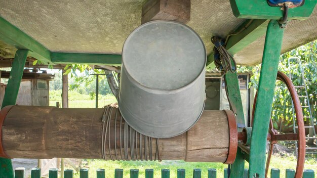 Un vecchio pozzo d'acqua con un secchio in giardino, una maniglia in metallo per sollevare l'acqua da terra. villaggio bene sotto il tetto con una corda. retro bene in campagna.