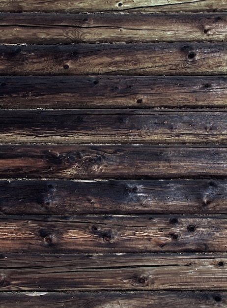 Old weathered log wall. Dark brown wooden background. Craked shabby logs.