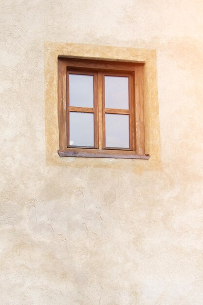 Old window with brown frame on the background of beige stone wall