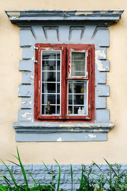 Old window with lattice. There are religious figurines behind the window. Paint on the frames and the walls is peeling.