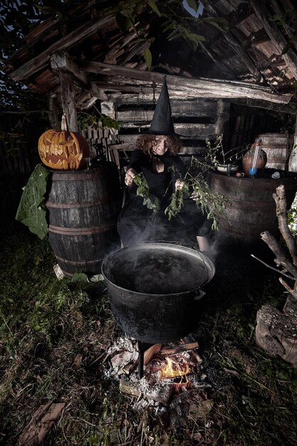 Old witch brewing deadly potion for halloween in a cast iron\
pot