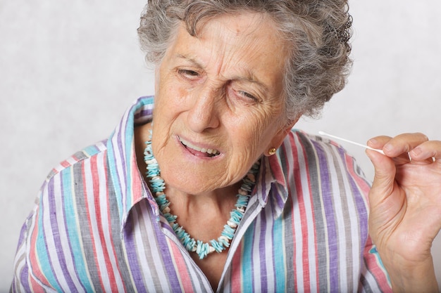 Old woman between 70 and 80 years old is cleaning her years with cotton swabs