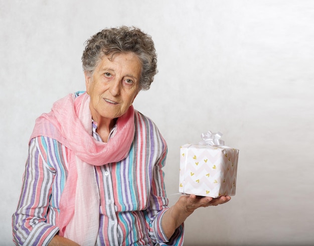 ピンクのスカーフと誰かからのプレゼントを身に着けた 70 ～ 80 歳くらいのおばあさん