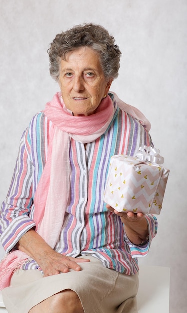 Пожилая женщина от 70 до 80 лет в розовом шарфе и чьем-то подарке