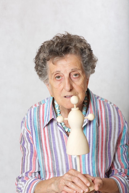 Old woman between 70 and 80 years old with mini wooden made mannequin