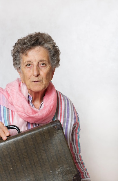 Old woman between 70 and 80 years old with pink scarf and vintage suitcase