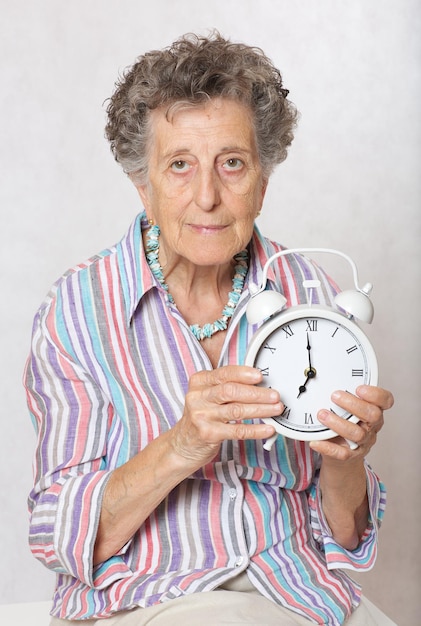 Photo old woman between 70 and 80 years old with vintage alarm clock