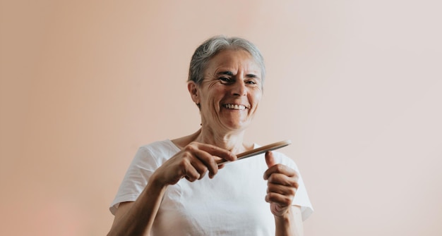 Old woman filing her nails,smiling removable flesh colored background.Elderly woman is getting a manicure.Woman prepare nails for gel polish filing gel down with filer.A woman makes her own manicure.