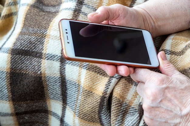 Vecchia donna mani con un telefono cellulare che chiama per la consegna o servizi di emergenza