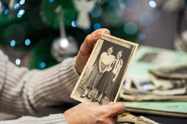 Old woman holding and old photo on Christmas tree background. Generations and life values concept.