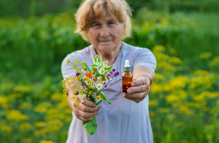 Photo an old woman holds an extract in a bottle of medicinal herbs and flowers selective focus nature
