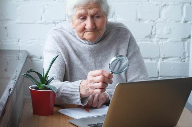 늙은 여자는 노트북 앞의 테이블에 앉아있다.
